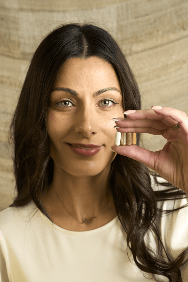 Closeup of a woman holding up 4 Nuwa Productivity capsules with one hand close to her face.